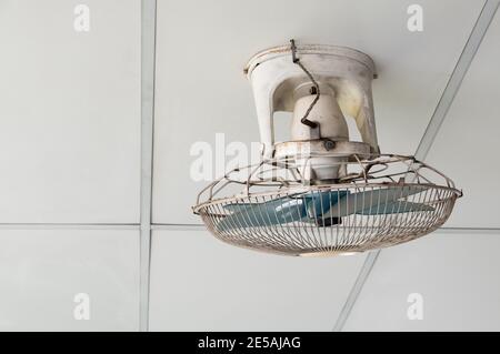 The old orbit fan with the many stains and dust is hanging on the ceiling of the relax area in the office building, for cool and ventilation in the su Stock Photo
