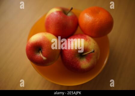 tangerine and three red apples in orange plate on the wooden table Stock Photo
