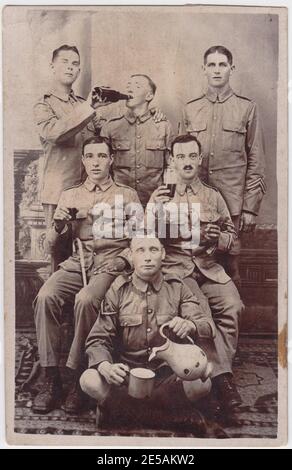 Informal group of six First World War soldiers. Five of the soldiers are shown with glasses, mugs and bottles of beer - one soldier is pouring the contents of a bottle into his companion. The sixth soldier is standing with his arms at his side, staring at the camera. Stock Photo