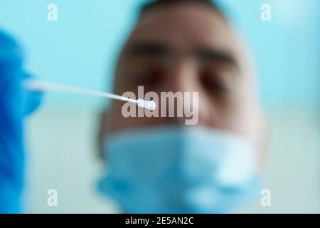 closeup of a healthcare worker, wearing blue surgical gloves, about to take a nasopharyngeal culture, using a swab, from the nose of a young man, wear Stock Photo