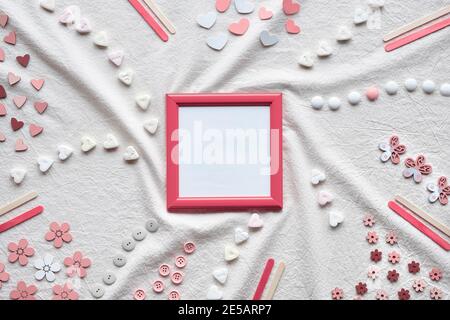 Abstract Springtime background. Pink picture frame with copy-space. Flat lay with hearts, candy, buttons, small decor arranged on textile background Stock Photo