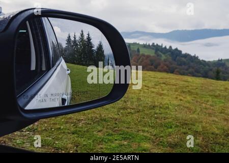 Reflection of pines in car side mirror close-up. Stock Photo