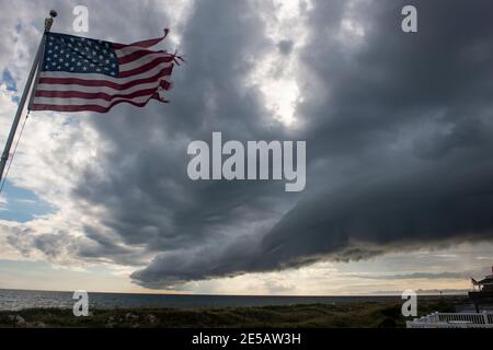A weather-beaten American flag blows as a shelf clouds appears on the leading edge of a storm in Atlantic Beach, North Carolina. Stock Photo