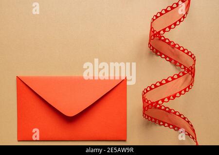 Valentine's day or Wedding romantic concept. Twisted decorative ribbon and red envelope with red hearts on beige background Stock Photo