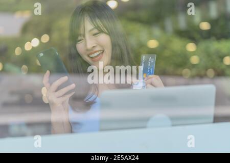 Asian woman using credit card with mobile phone for online shopping in modern coffee shop, technology money wallet and online payment concept, credit Stock Photo