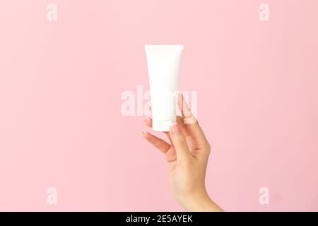 Woman holding cream tube and applying moisturizer lotion on her beautiful hands for soft and healthy skin on pink background Stock Photo
