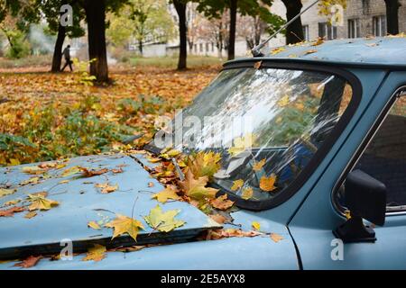 Yellow leaves on the old retro car. Vintage broken auto under trees in the park in fall season. Kharkiv, Ukraine Stock Photo