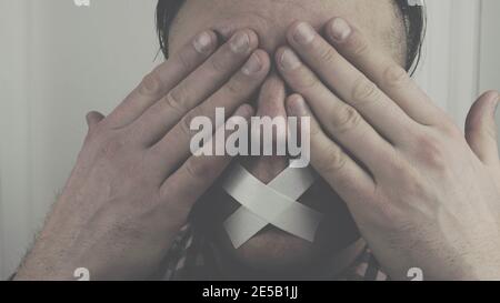A man covers his eyes with his hands, a man with a sealed mouth and closed eyes. Stock Photo
