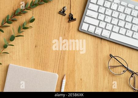 Wood office desk with keyboard, notebook, glasses, eucalyptus branches. Modern feminine workspace concept. Flat lay, top view. Stock Photo