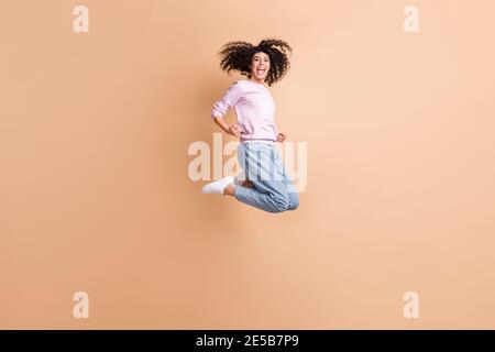 Full size profile photo of hooray jump curly girl wear sweater jeans sneakers isolated on peach color background Stock Photo