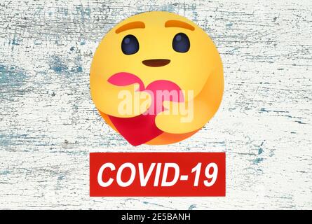 Kiev, Ukraine - August 25, 2020: Facebook new Care Empathetic Emoji Reaction with Covid-19 label on wooden background. Facebook is adding a hug reacti Stock Photo