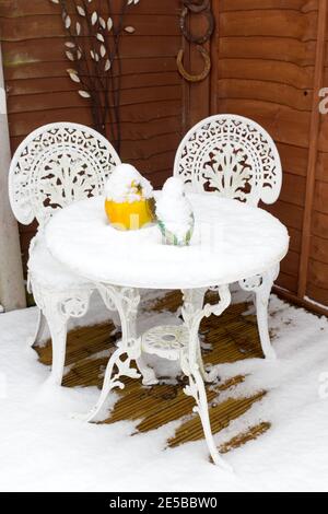 close up of patio table and chairs covered in snow on decking.  bird ornaments on table are covered in snow Stock Photo