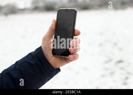 close up of man's hand holding black mobile phone device outside in snow in winter time Stock Photo
