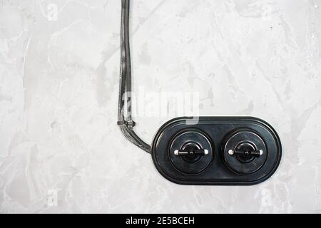 A black old-fashioned switch with wires is mounted on a gray concrete wall. Electric switch with two vintage switches. Stock Photo