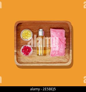 Isolated a wooden tray with piece of homemade flower soap, herbal shower gel and oil capsules on a trendy color background. Natural beauty products fo Stock Photo