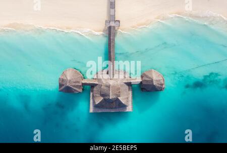 Aerial shot of the Stilt hut with palm thatch roof washed with turquoise Indian ocean waves on the white sand sandbank beach on Zanzibar island, Tanza