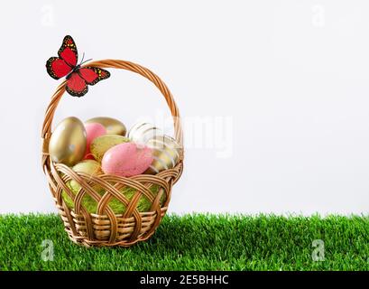 Basket full of multicolored easter eggs on green meadow over white background. Easter greeting card. Stock Photo