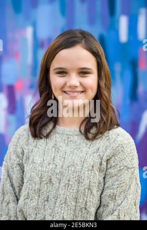 Young girl wearing a sweater in the winter standing outside near a bright colored wall with blue, pink, and purple. Stock Photo