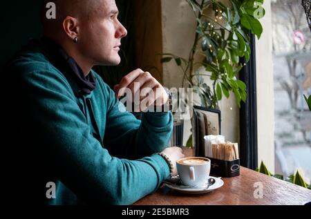 Young man in a cafe, leaning on his elbows with a cup of coffee in front of him. Concept of being alone. Stock Photo