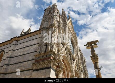 Left side of the Siena Cathedral (Saint Mary of the Assumption) in Romanesque-Gothic style with the Siennese Wolf on a column, Tuscany, Italy Stock Photo