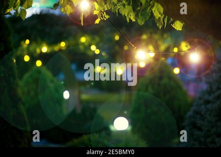 illumination holiday lights glare on garden with electric garland bulbs of warm light glow with round bokeh evening illuminate night scene of outdoor Stock Photo