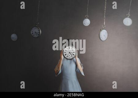 woman with face hidden by a clock in a room full of grandfather clocks Stock Photo