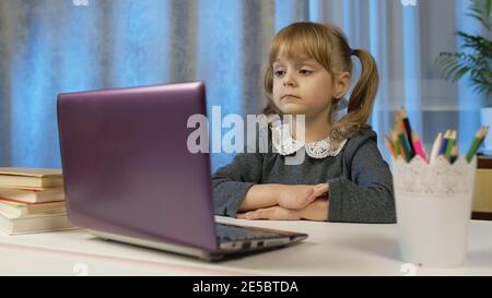 Child girl doing school homework, writes in notebook, using laptop computer at home. Back to school, online learning, distance lesson, pupil education at home, technology for schoolgirl. Slow motion Stock Photo
