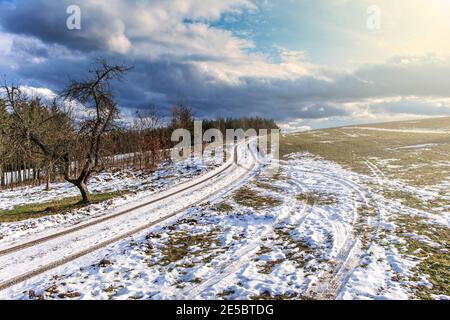 Thawed on the field with snow against sky.   Landscape in Czech Republic. Melting snow in fields and around trees. Tire tracks in the snow. Stock Photo