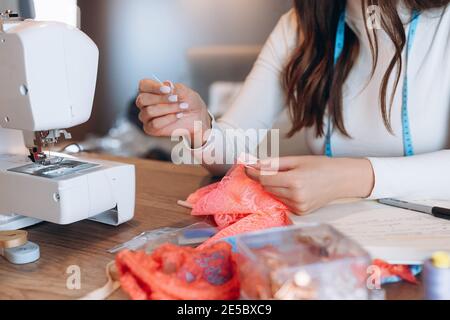 Close up young dressmaker woman working on sewing machine. Hand of the seamstress is using a needle. Creating online clothing design courses. Stock Photo