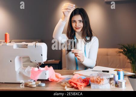 Young dressmaker woman sews clothes on sewing machine. Using a needle seamstress in workshop. Creating online clothing design courses. Stock Photo