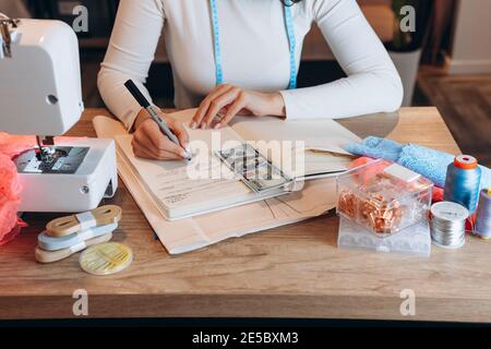 Tailoring, sewing and clothing concept - close up of female fashion designer writing down ideas or salary. Stock Photo