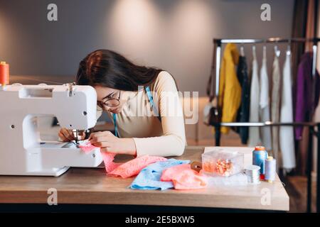 Premium Photo  Young dressmaker woman sews clothes on sewing machine.  holding tape measure in workshop. creating online clothing design courses.