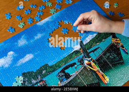 Hand of middle aged woman completing a jigsaw puzzle of Longtail boats in Thailand Stock Photo