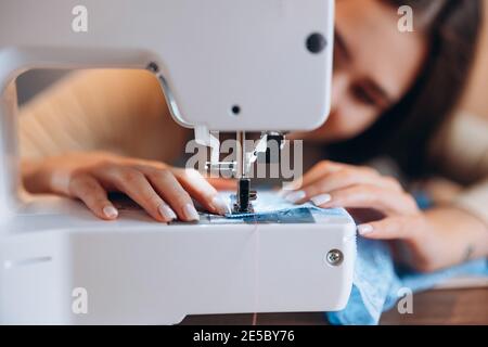 Young dressmaker woman sews clothes on sewing machine close-up. Creating online clothing design courses. Stock Photo