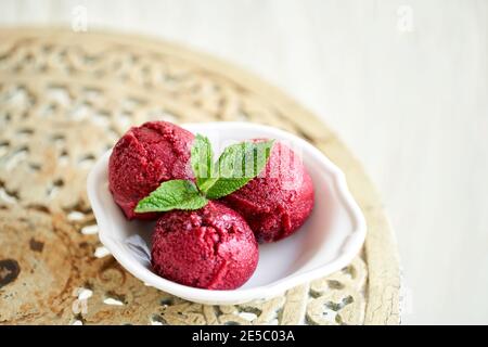 Berry ice cream with mint leaf. three balls in a white bowl on a vintage table. sorbet Stock Photo
