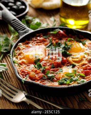 Close up view of a traditional shakshouka dish made of tomatoes and eggs served in a cast iron pan  on a wooden table Stock Photo