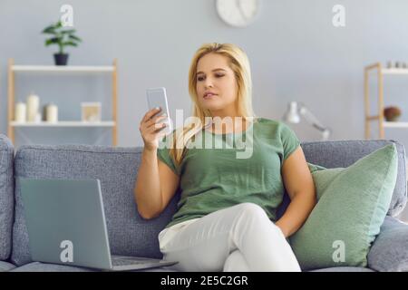 Woman working from home using laptop computer while reading text message on mobile phone. Stock Photo