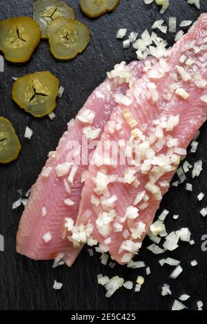 Traditional dutch maties herring with chopped onion and pickled cucumber on a dark background top view Stock Photo