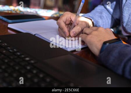 selective focus of a young student taking notes in a notebook with the computer and cell phone on the table Stock Photo