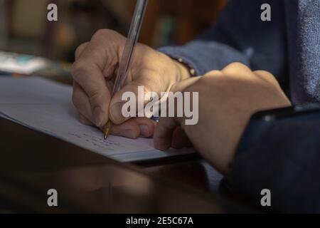 Close-up of a teenager's hands writing with a pen on a notebook placed on a wooden desk. Stock Photo