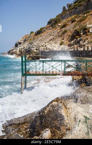 Sea water beats against rocky rocks and makes waves with foam, rugged pier in the sea Stock Photo