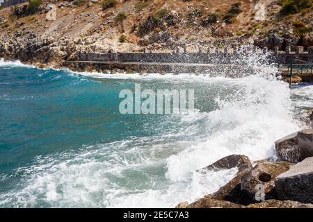 Sea water beats against rocky rocks and makes waves with foam, rugged pier in the sea Stock Photo