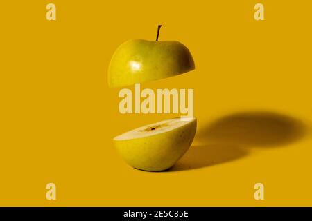 Green apple sliced in half with one half floating in air. Dark yellow background. Creative fruit concept Stock Photo