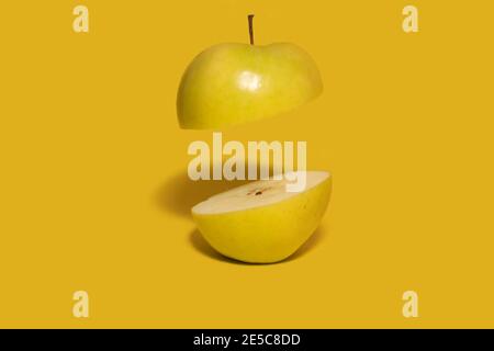 Green apple sliced in half with one half floating in air. Dark yellow background. Creative fruit concept Stock Photo