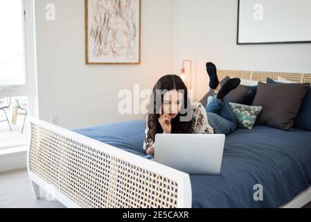 Young woman lying on bed looking at laptop Stock Photo