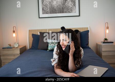 Happy young woman talking on phone in bedroom Stock Photo