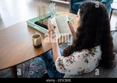 Woman sitting on floor next to coffee table reading book Stock Photo