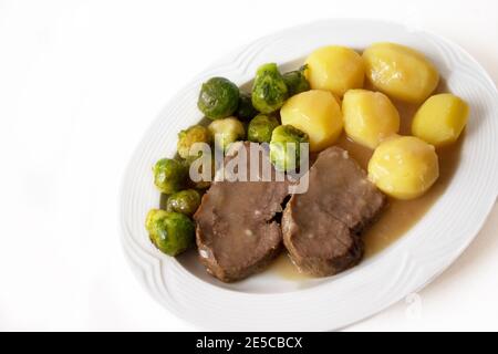 Slices of beef roast with boiled potatoes, brown sauce and fresh sprouts isolated on white background