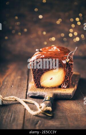 Homemade chocolate cake with pear at rustic wooden background with bokeh. Christmas brownie with fudge. Selective focus. Stock Photo