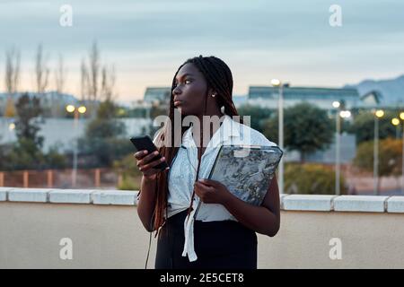 Young african student is using her mobile and is holding a folder Stock Photo